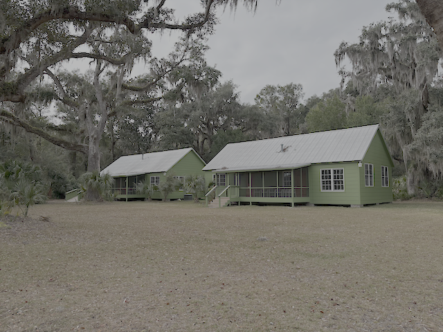 Two cabins, painted green, with a grassy lawn in front and live oaks with Spanish moss framing the photo.