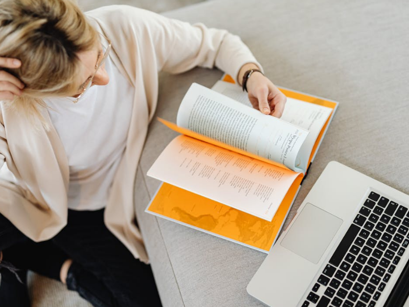 woman with hand on head and open book and laptop looking confused or trying to understand something