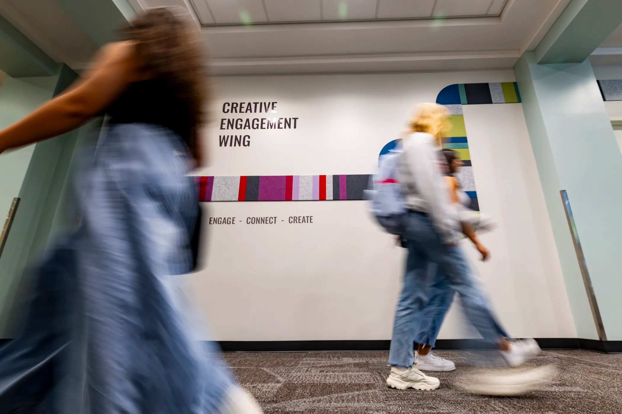 Blurred students walk by Creative Engagement Wing sign