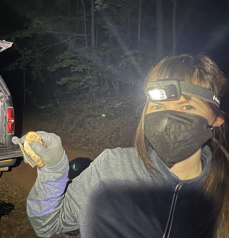 Marisa Mizzoni, wearing a head lamp and a mask, holding a bat