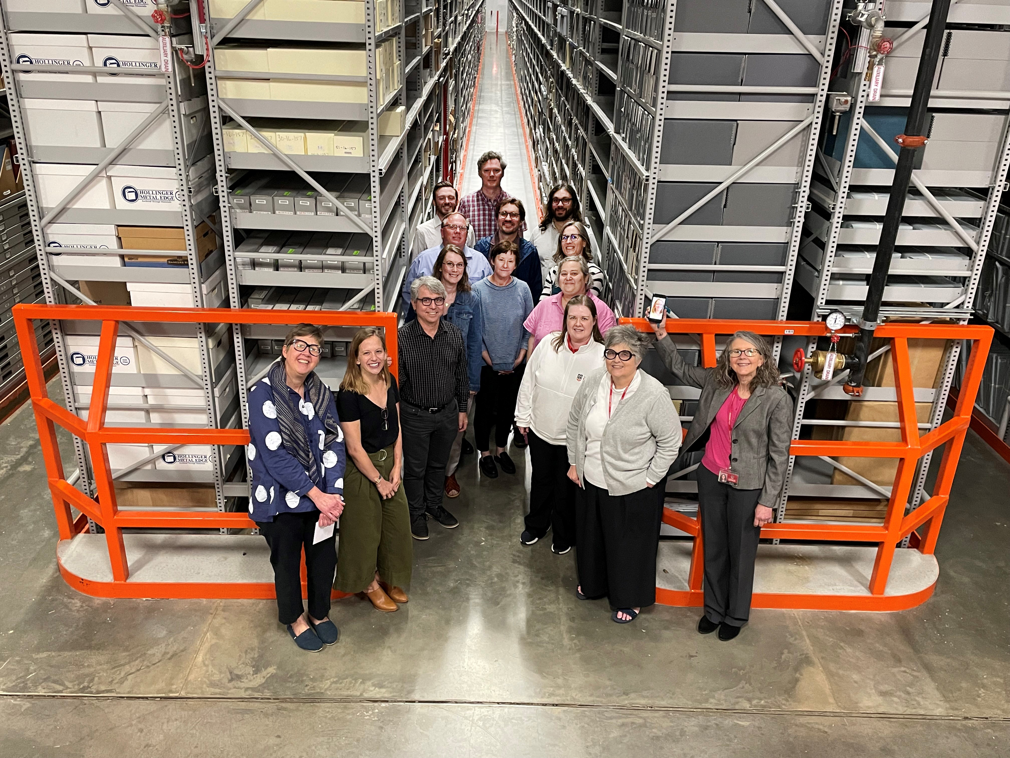 A group of faculty members smiling at the camera while in between large shelves in a vault