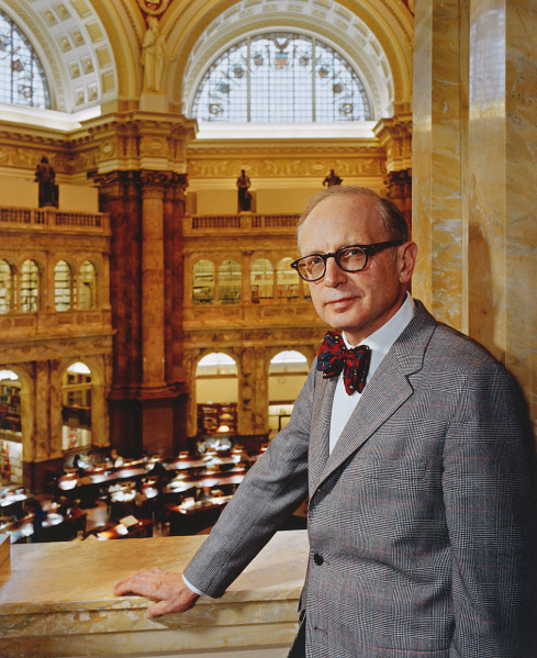 Photo of Daniel Boorstin, a middle-aged man in a grey suit with a tartan bowtie, on a balcony in the Library of Congress
