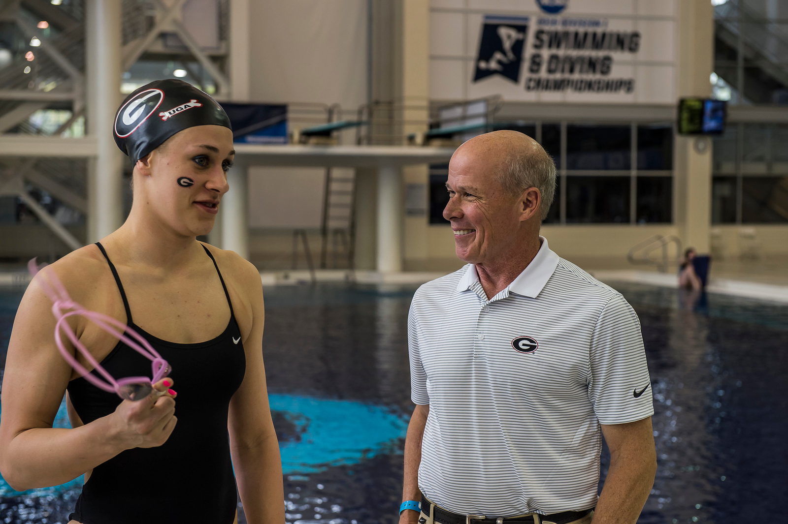 woman with swim cap on talks to coach in front of pool