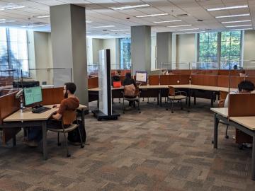 Students sit at computers in an area of curved tables. Some seats have computers, others do not. 