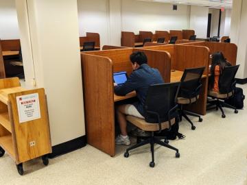Students sit at individual cubicles, working on their laptops