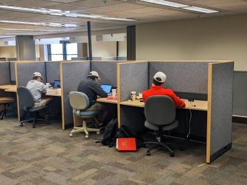 Several students sit at individual cubicles, studying